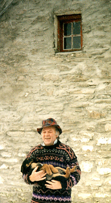A man with a hat laughing with an upturned puppy in his arms.