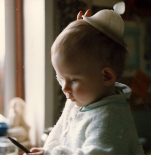 Baby looking at a pencil while a stone hat slips from her head.